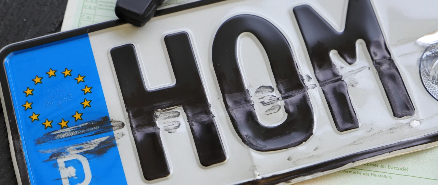 Close-up of a damaged car number plate with scratches and dents, highlighting the need for a damaged number plate replacement.