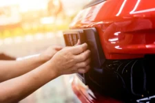 Close-up of a person attaching a car number plate to a red bumper without screws, using adhesive pads.