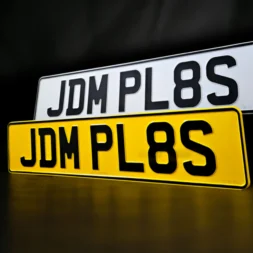 A pair of pressed metal number plate showcasing the registration number 'JDM PL8S'.
