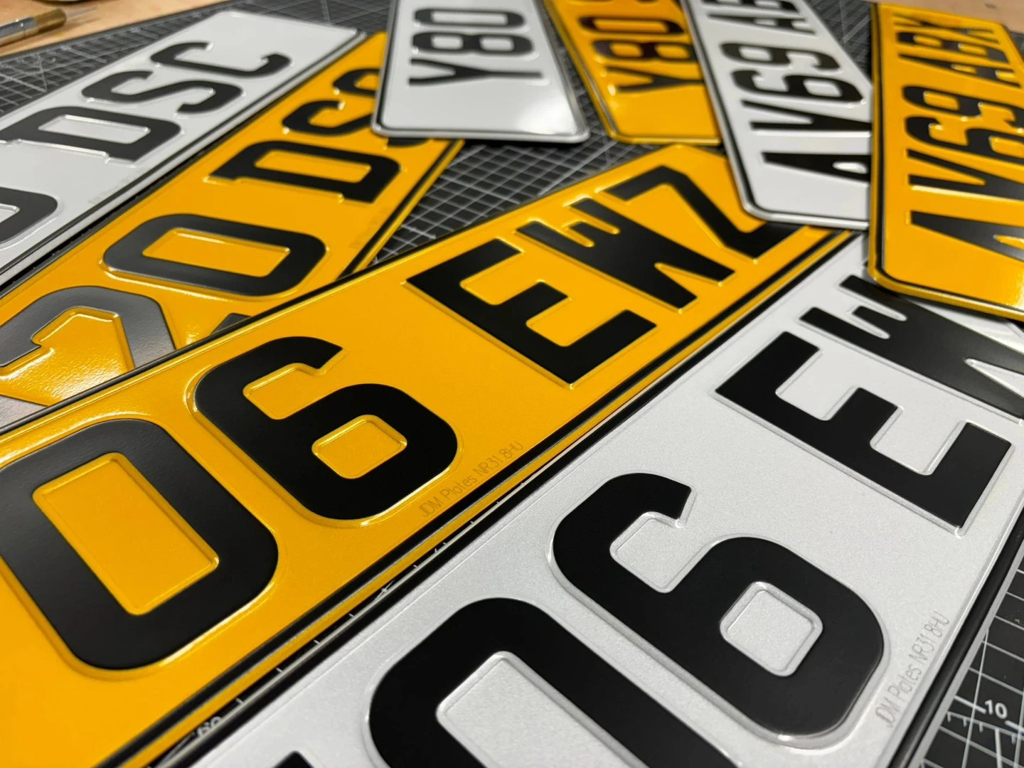 Close-up view of several UK vehicle registration plates, both yellow rear plates and white front plates, scattered on a cutting mat.