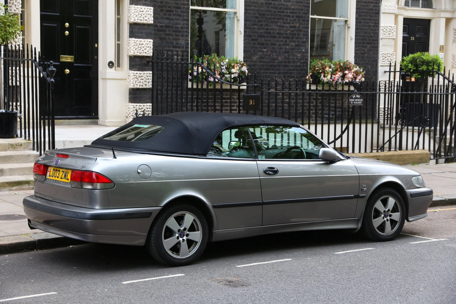 Silver Saab 9-3 SE convertible with black soft top parked on a city street.