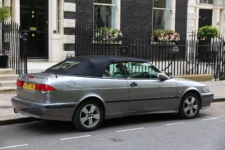 Silver Saab 9-3 SE convertible with black soft top parked on a city street.