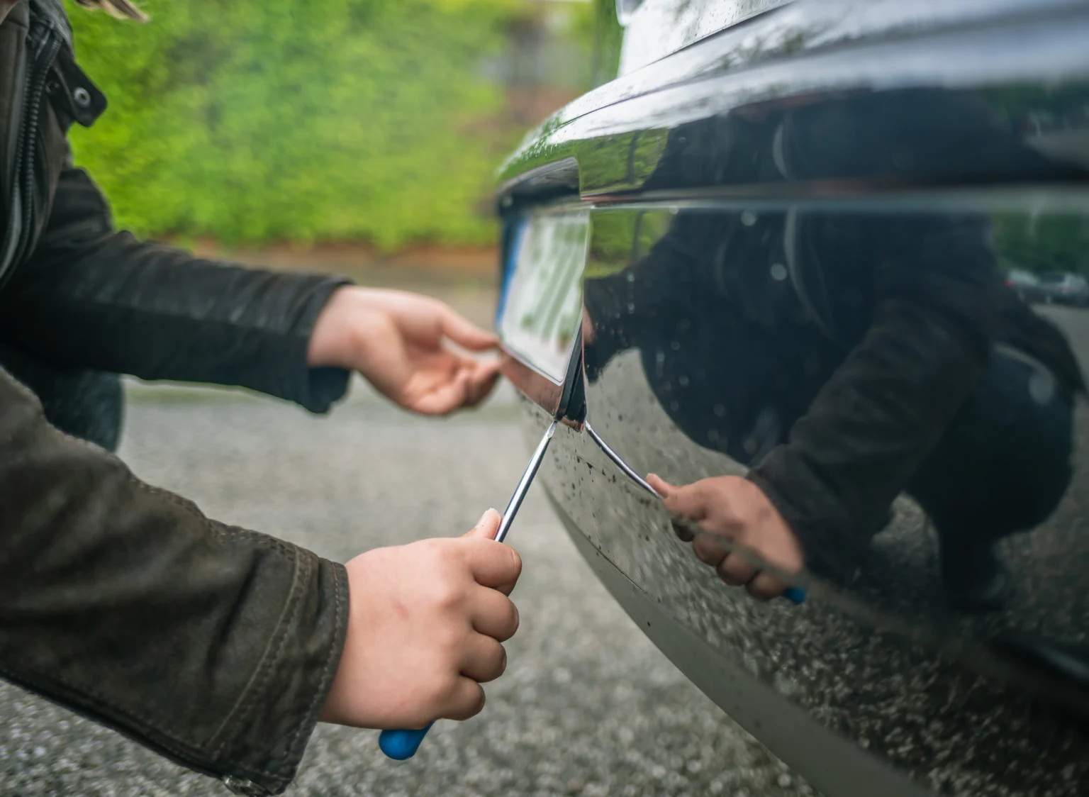 A person using a screwdriver to steal a car’s number plate in a quiet residential area, illustrating a common method of number plate theft