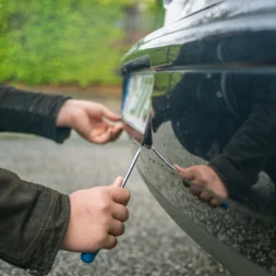 A person using a screwdriver to steal a car’s number plate in a quiet residential area, illustrating a common method of number plate theft