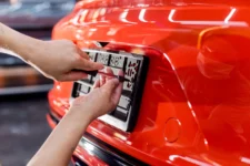 Hands fixing number plate frame to front of red high-performance car in showroom