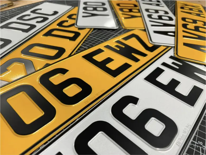 Close-up of multiple replacement car number plates from JDM Plates, including yellow rear and white front plates with raised 3D lettering.